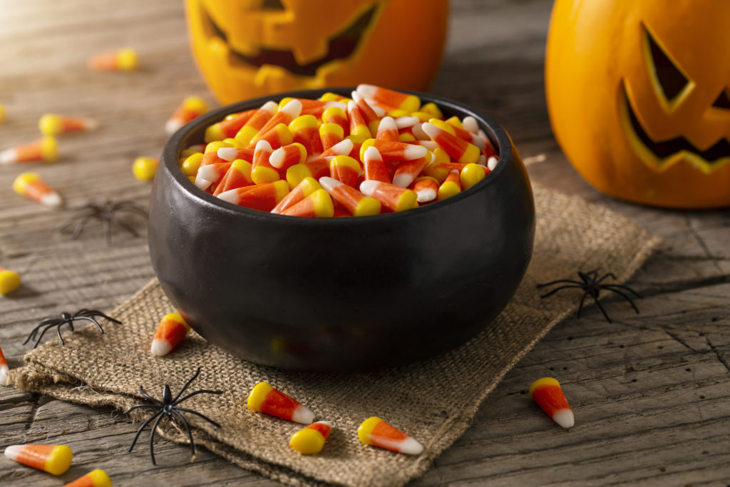 Bowl of candy corn surrounded by jack-o-lanterns and plastic spiders